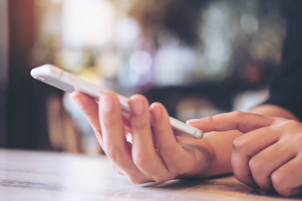 Closeup image of a woman's hands holding , using and pointing at smart phone in modern cafe